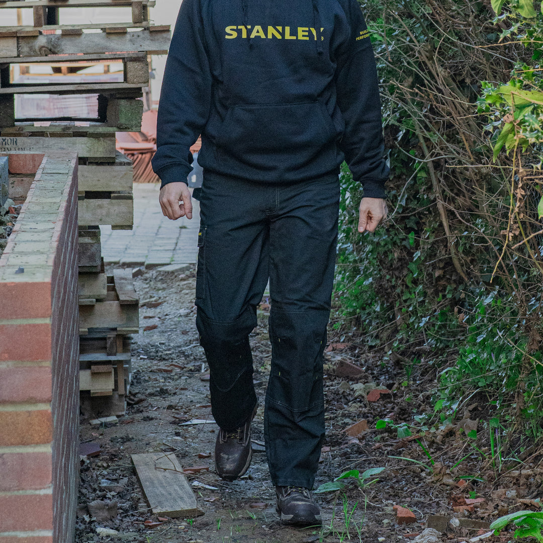 Person wearing a Stanley jacket walking outdoors near construction materials.