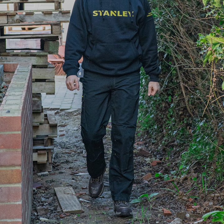 Person wearing a Stanley jacket walking outdoors near construction materials.